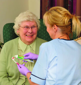 A dental nurse helping an elderly patient with toothbrushing.